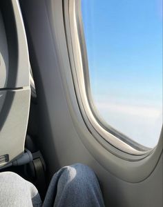 the view from inside an airplane looking out at the clouds and blue sky, with someone's feet propped up on the seat