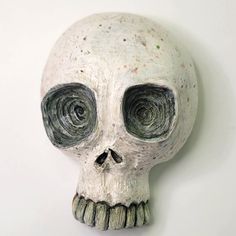 a white skull with two large eyes on it's face, against a white wall