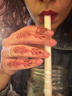 a woman holding a straw in her hand with henna tattoos on it's fingers