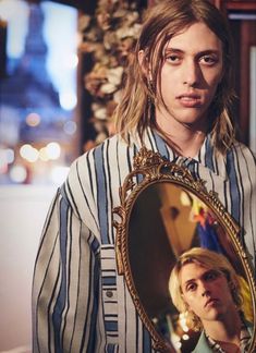 a man with long hair holding a mirror in front of his face and looking at the camera