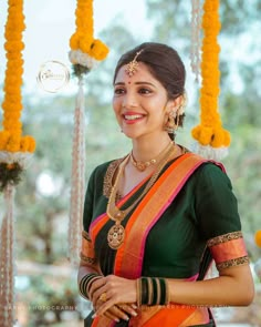 a woman in an orange and green sari smiles at the camera while standing under yellow flowers