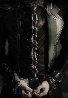 a man dressed in black and green is holding his hands together with chains attached to the chest