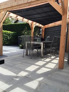 an outdoor dining area with table and chairs under a pergolated roof, surrounded by greenery