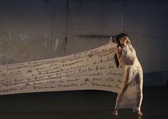 a woman in a white dress talking on a cell phone while holding a piece of paper with writing on it