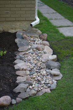 a rock garden bed in front of a house with green grass and rocks on the ground