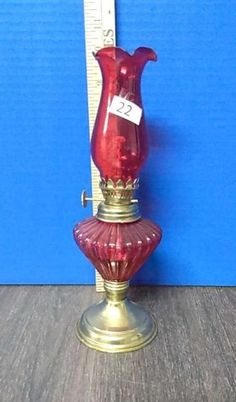 a red glass vase sitting on top of a table next to a measuring tape holder