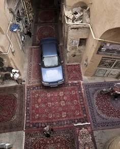 an overhead view of a car parked in the middle of a narrow alleyway with rugs on both sides