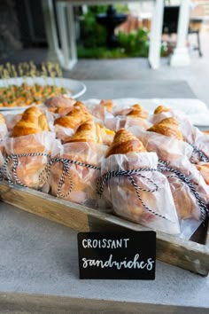 many croissant sandwiches wrapped in plastic wrap are on display at the storefront