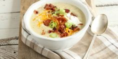 a white bowl filled with soup on top of a wooden table next to a spoon