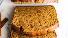 slices of pumpkin bread sitting on top of a white cutting board next to cinnamon sticks