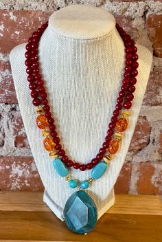 Agate Ambrosia Statement Necklace Genuine Scarlet Jade Genuine Amber Resin Genuine Agate Genuine Turquoise Magnesite Gold-Tone Metal Lobster Claw Clasp Crafted and Finished by Hand Approximate Measurements: Length- 17" + 2" Extender; Pendant is 2.25" in Length and 1.5" in Width Adorn yourself with the mesmerizing beauty of the Agate Ambrosia Statement Necklace! Crafted from genuine Scarlet Jade, Amber Resin, Agate, and Turquoise Magnesite, each stone is lovingly encased in a gold-tone metal sett Turquoise Agate Faceted Bead Necklaces, Turquoise Agate Faceted Beads Necklace, Turquoise Agate Necklace With Faceted Beads, Turquoise Agate Gemstone Beaded Necklaces, Turquoise Agate Beaded Necklace With Gemstones, Turquoise Agate Gemstone Beaded Necklace, Turquoise Agate Beaded Necklace, Turquoise Double Strand Gemstone Jewelry, Turquoise Agate Gemstone Jewelry