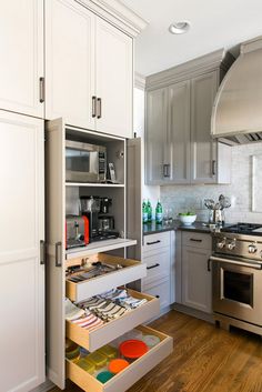 an open drawer in the middle of a kitchen with white cabinets and stainless steel appliances