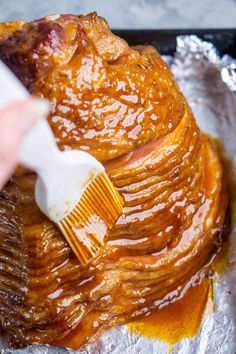 someone using a brush on some food that is sitting on tin foil in the oven