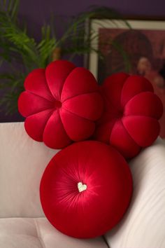 three red pillows sitting on top of a white couch next to a potted plant