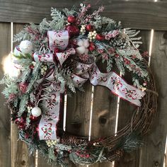 a christmas wreath hanging on the side of a wooden fence with red and white decorations