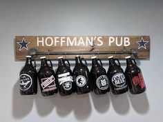 a wooden sign hanging from the side of a wall with six beer bottles on it