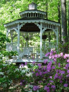 a white gazebo surrounded by purple flowers and trees