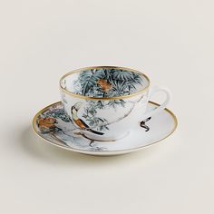 a tea cup and saucer with birds on the rim, sitting next to each other