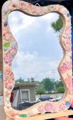 a hand holding up a mirror with seashells on it