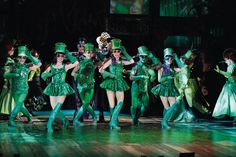 a group of people that are on stage with some green outfits and hats in the air