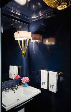 a bathroom with blue walls and white counter tops, gold fixtures and a chandelier