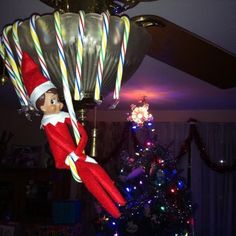 an elf is hanging from the ceiling with some candy canes in his hand and on top of a christmas tree