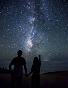 two people are standing under the stars in the sky with their hands up to each other