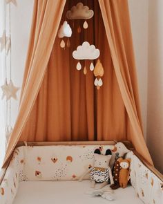 a baby crib with an orange drape and white clouds hanging from the ceiling