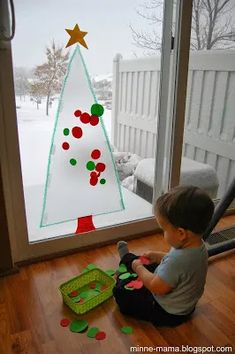 a young boy sitting on the floor in front of a window with a christmas tree drawn on it