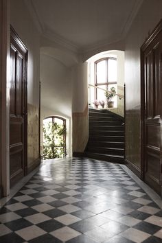 an empty hallway with black and white checkered flooring, two doors leading to another room