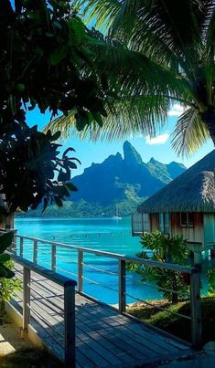 a wooden walkway leading to a beach with mountains in the background and blue water on both sides