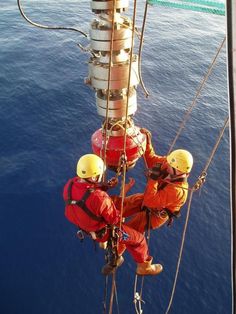 two men in orange work on the side of a boat