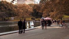 people are walking around in the park with umbrellas and sailboats on the water