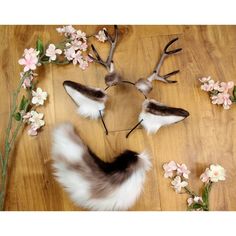 two deer head made out of fake fur and flowers on a wooden floor next to a pair of antlers