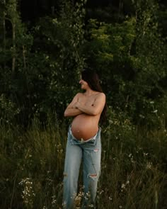 a pregnant woman standing in tall grass with her arms crossed