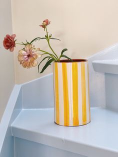 a yellow and white striped vase with flowers in it sitting on a shelf next to stairs