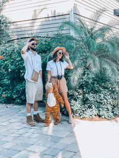 a man and woman are standing in front of some bushes with a small child dressed as a tiger