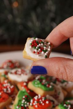 a person is holding up some cookies with sprinkles on them in front of a christmas tree