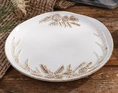 a white and gold plate sitting on top of a wooden table next to a plant