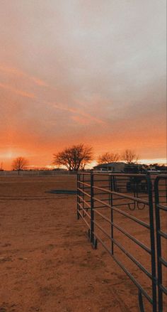 the sun is setting behind a fence in an open field with cattle grazing on it