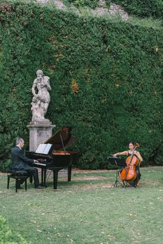 two men playing instruments in front of a statue and a piano on the grass outside