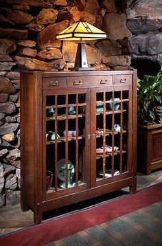 a lamp on top of a wooden cabinet in front of a stone wall and potted plants