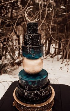 a three tiered cake sitting on top of a black tablecloth covered in snow