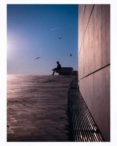 a man sitting on top of a bench next to the ocean under a blue sky