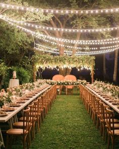 an outdoor wedding reception setup with string lights and wooden chairs, greenery on the lawn