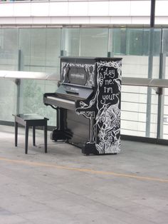 a black piano sitting in front of a glass wall next to a bench and table