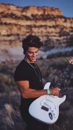 a man is holding an electric guitar in the desert