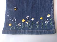 a blue jean with daisies and bees embroidered on the side, sitting on a white surface