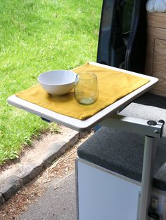 a bowl and glass on a table in the back of a van with grass behind it