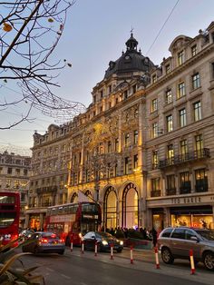 cars, buses and double decker buses are driving down the street in front of buildings